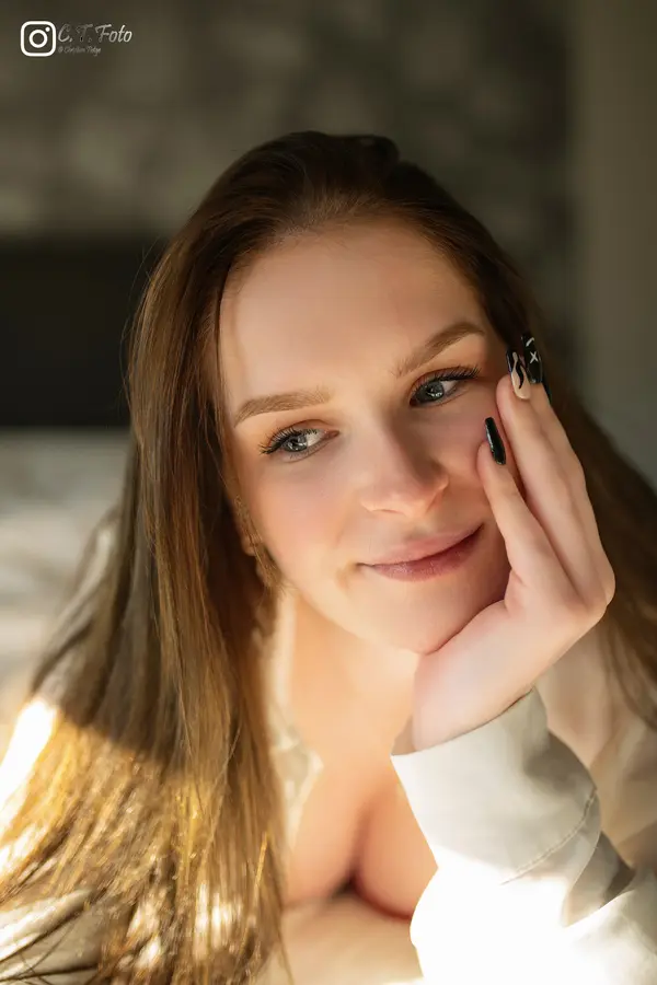 Frau liegt auf dem Bett und stützt das Kinn auf – warmes Fensterlicht Portrait